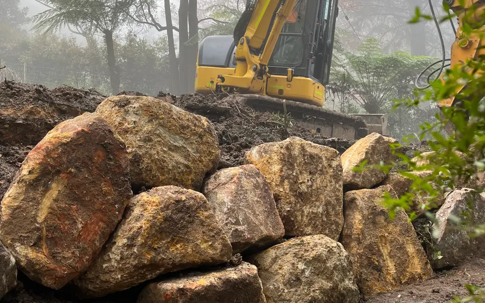 Long charcoal concrete sleeper retaining wall with gravel drainage strip and lawn