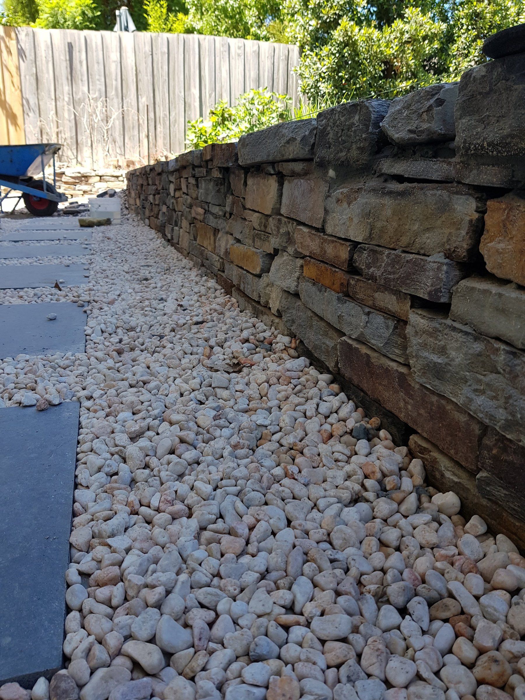 Curved rock retaining wall and pebble path